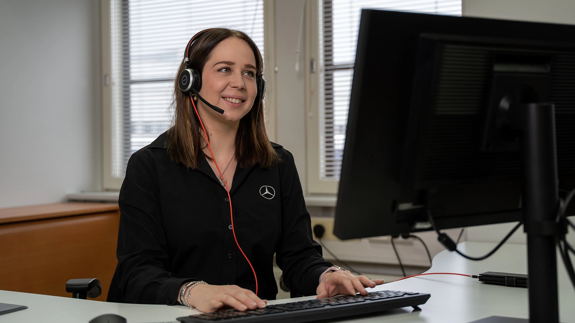 Asiakaspalvelussa työskentelevä nainen istuu tietokoneen edessä kuulokkeet päässä.