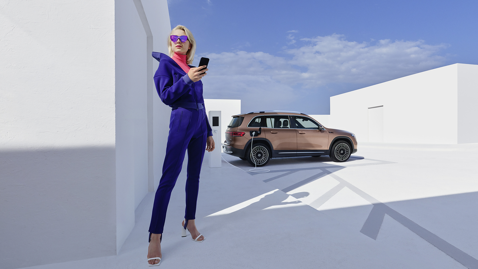 Henkilö puhelin kädessä, taustalla Mercedes-Benz EQB.