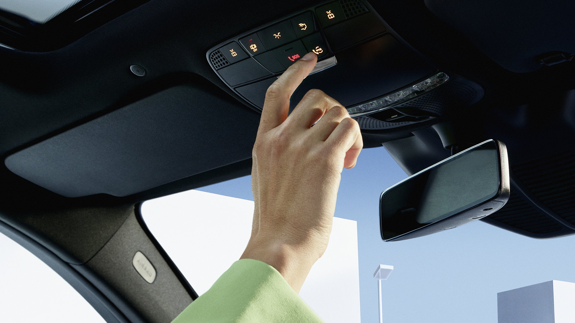 Kuvassa käsi, joka painaa auton kattoyksikössä sijaitsevaa Mercedes me-nappia.