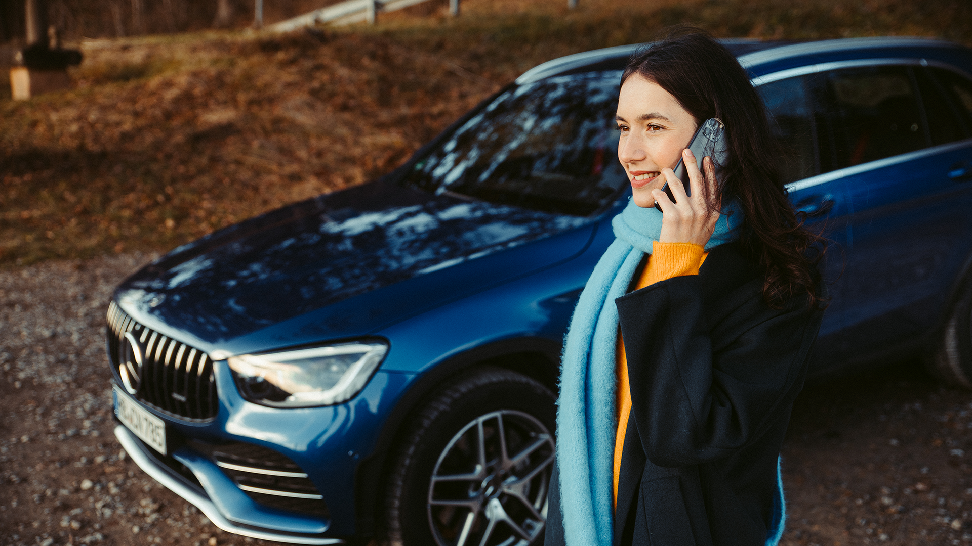 Henkilö Mercedeksen vieressä puhuu puhelimessa.